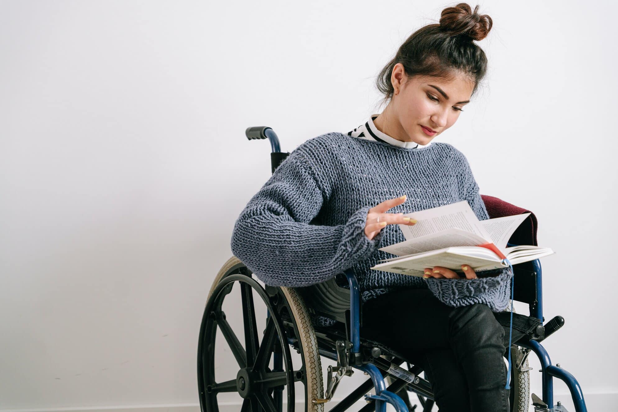 A lady with brittle bones is sat in a wheelchair, she is researching from a book information regarding disability counselling